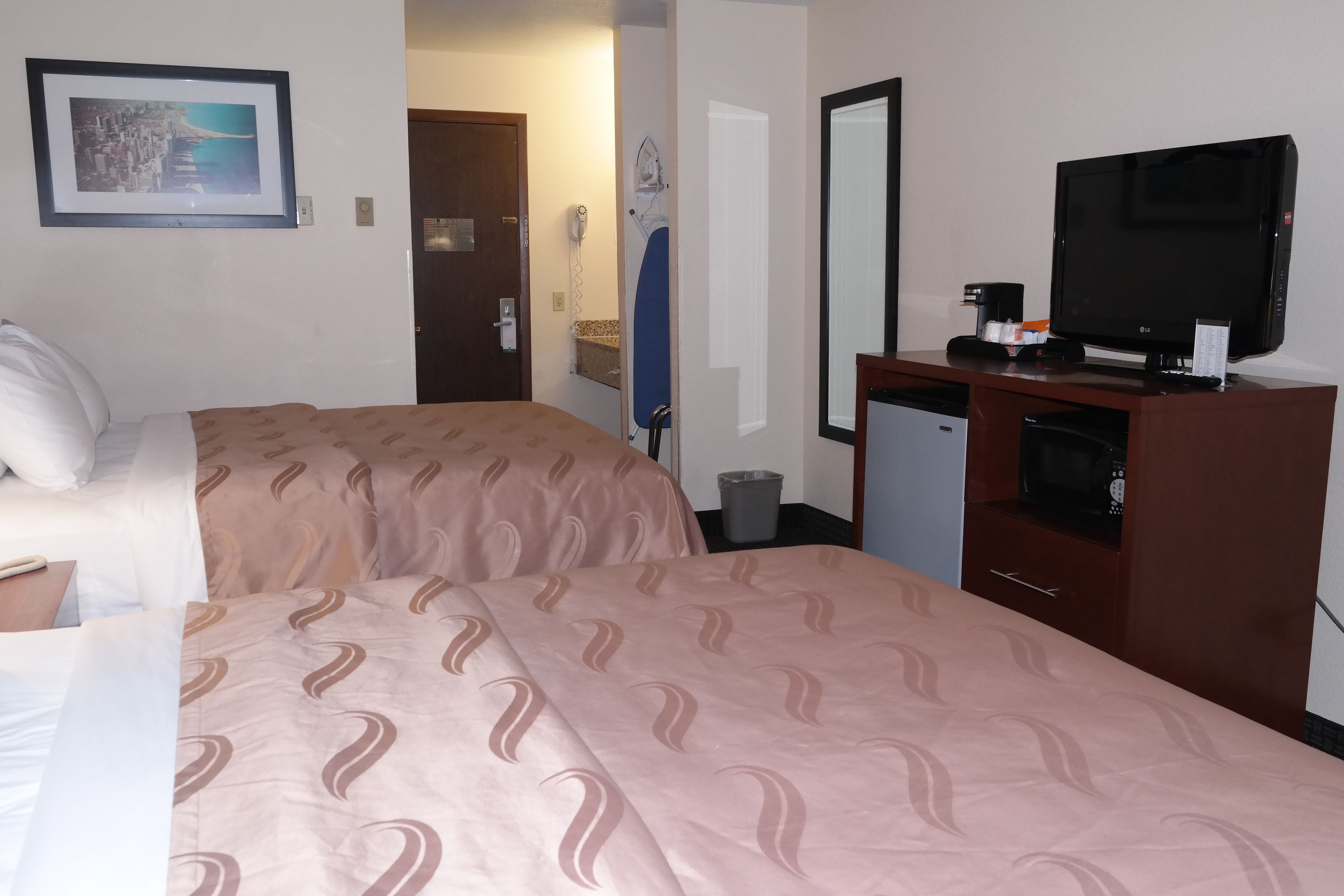 A hotel room with two beds, a television, a small refrigerator, and a mirror.