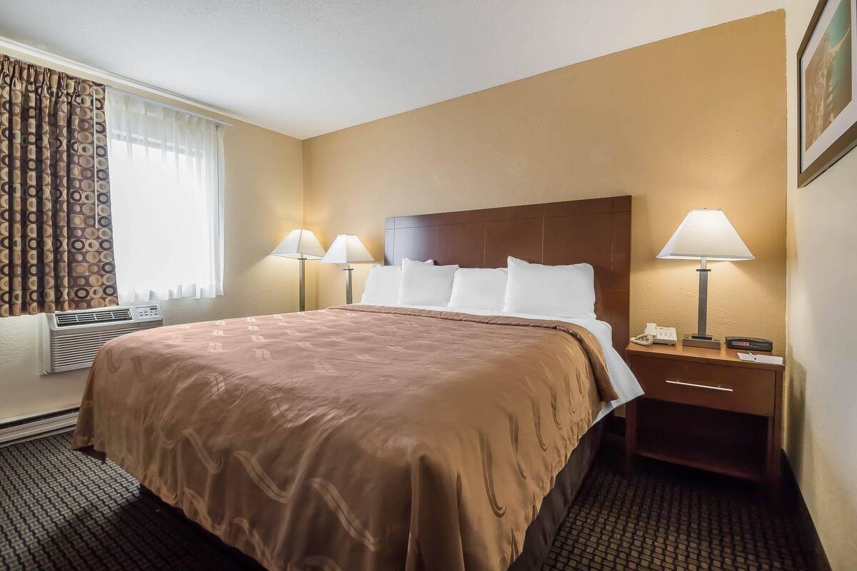 A hotel room with a large bed, two bedside lamps, a nightstand, and a wall-mounted phone.