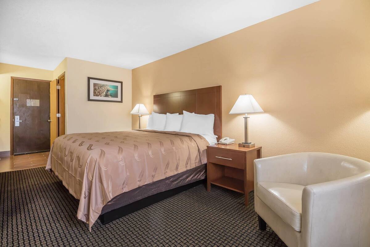 A hotel room with a bed, bedside lamps, a chair, a nightstand, and a door.