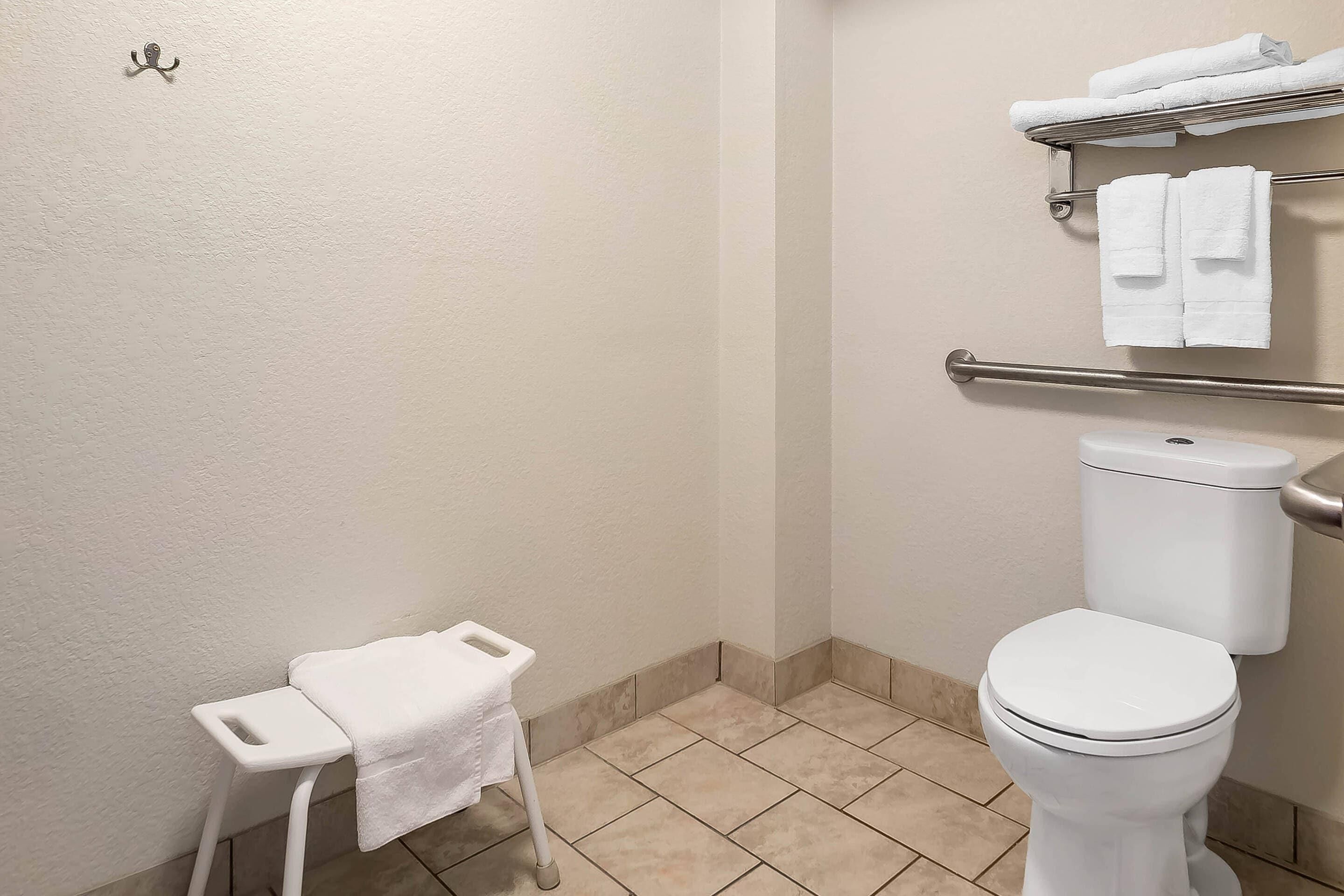A bathroom with a white toilet, a small white bench with a towel, and a towel rack above the toilet.