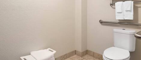 A bathroom with a white toilet, a small white bench with a towel, and a towel rack above the toilet.