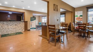 A hotel lobby with a reception desk, wooden chairs, and a green mat.