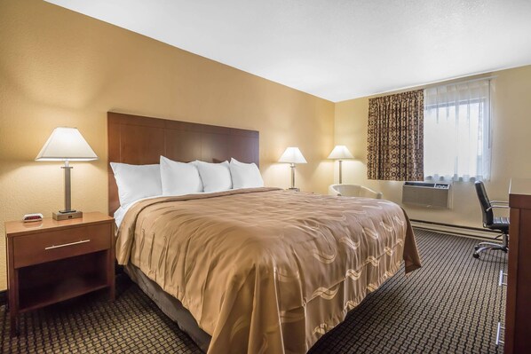 A hotel room with a bed, bedside lamps, a desk, a chair, and a window with curtains.