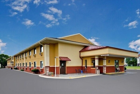 Situated on a flat, paved area, this two-story motel features a covered front porch with seating and windows along the upper level.