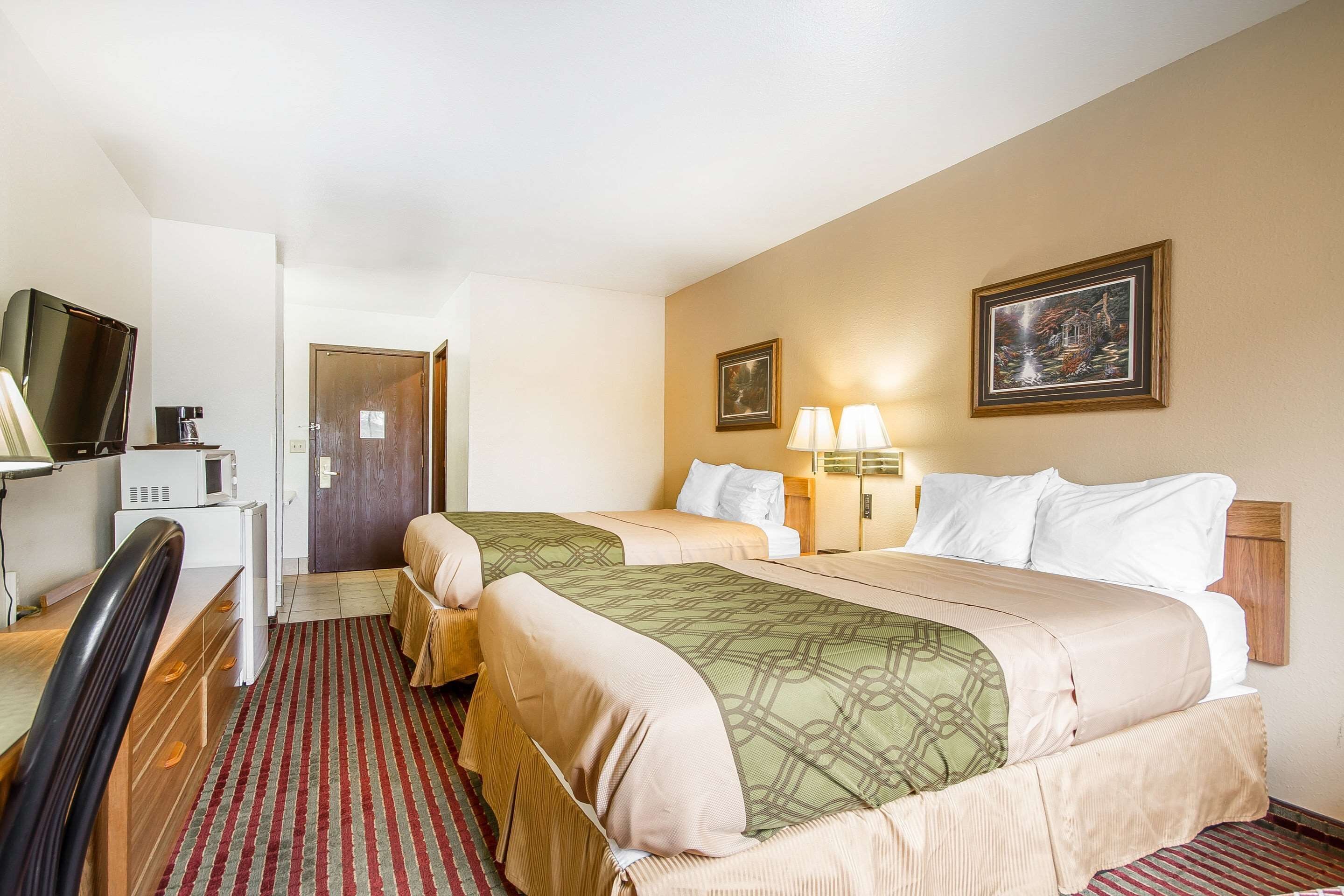 A hotel room with two beds, a desk with a chair, a television, and a microwave.