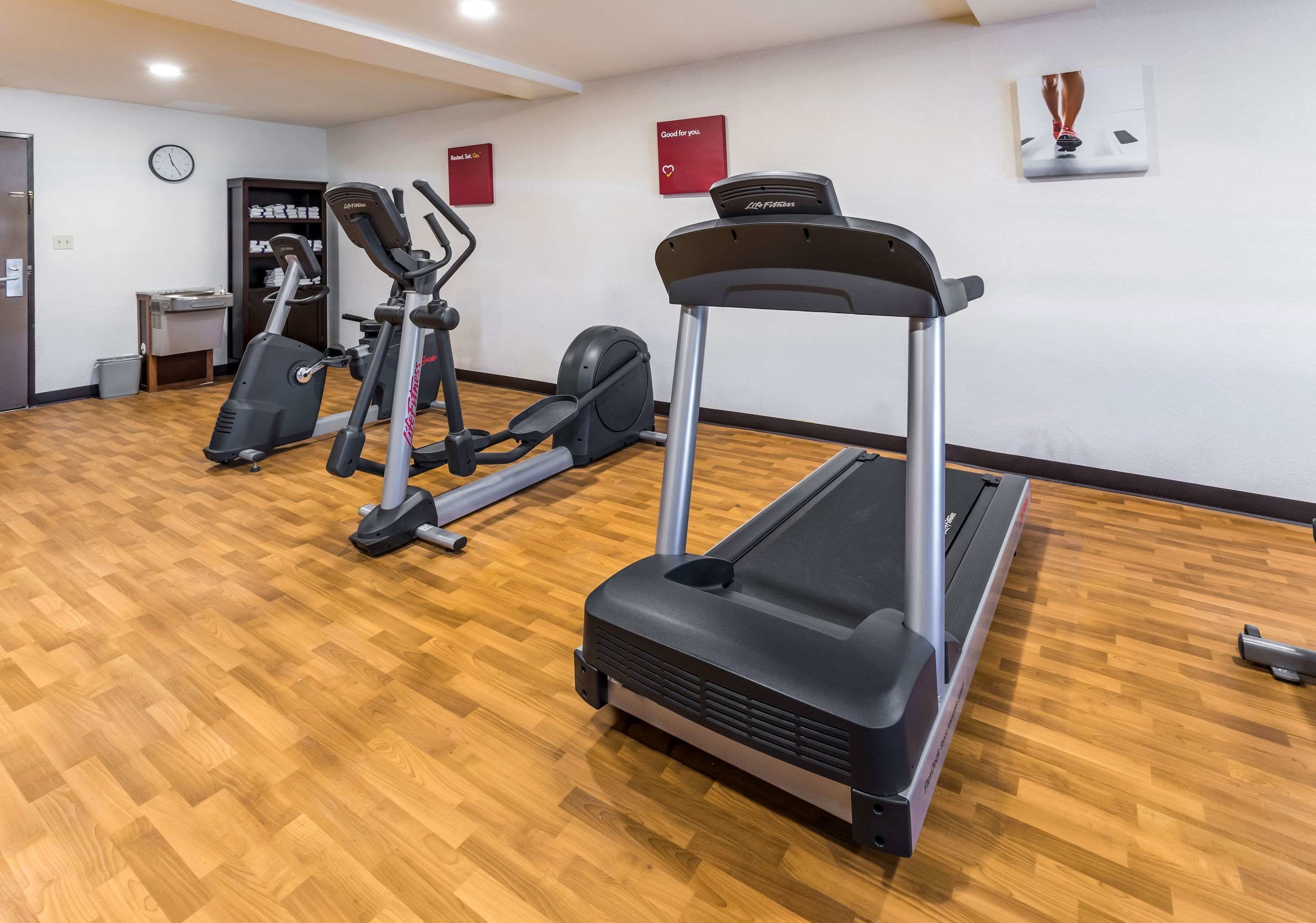 Un gimnasio con cintas de correr, bicicletas estáticas y máquinas elípticas sobre un piso de madera.