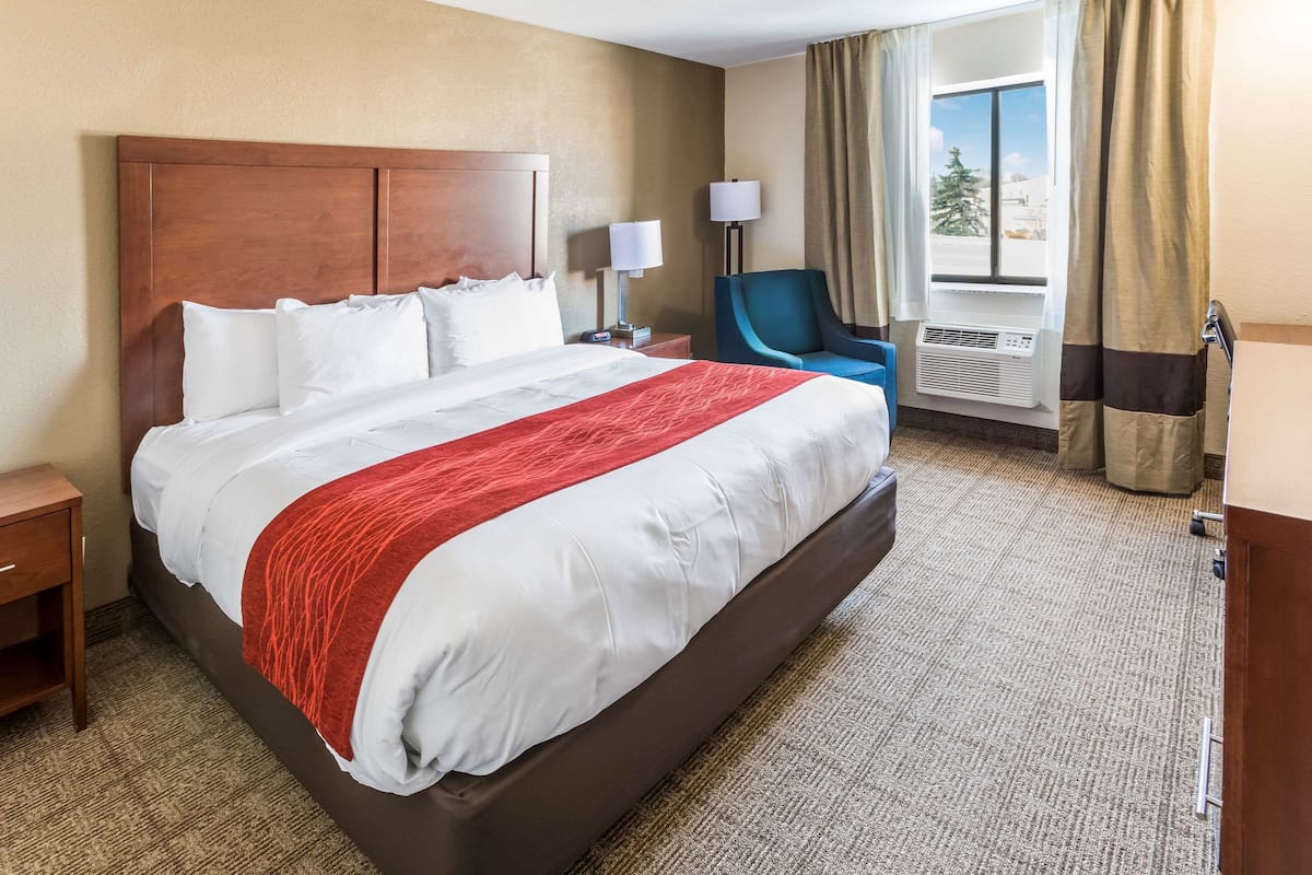 Une chambre d’hôtel avec un grand lit, une table de chevet, une chaise, une lampe et une fenêtre avec des rideaux.