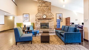 A lobby with a stone fireplace, blue sofas, a patterned rug, and a clock on the wall.