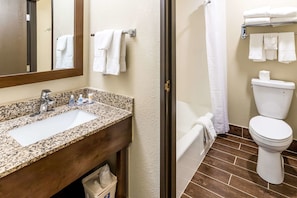 A bathroom with a granite countertop sink, a toilet, and a shower area.