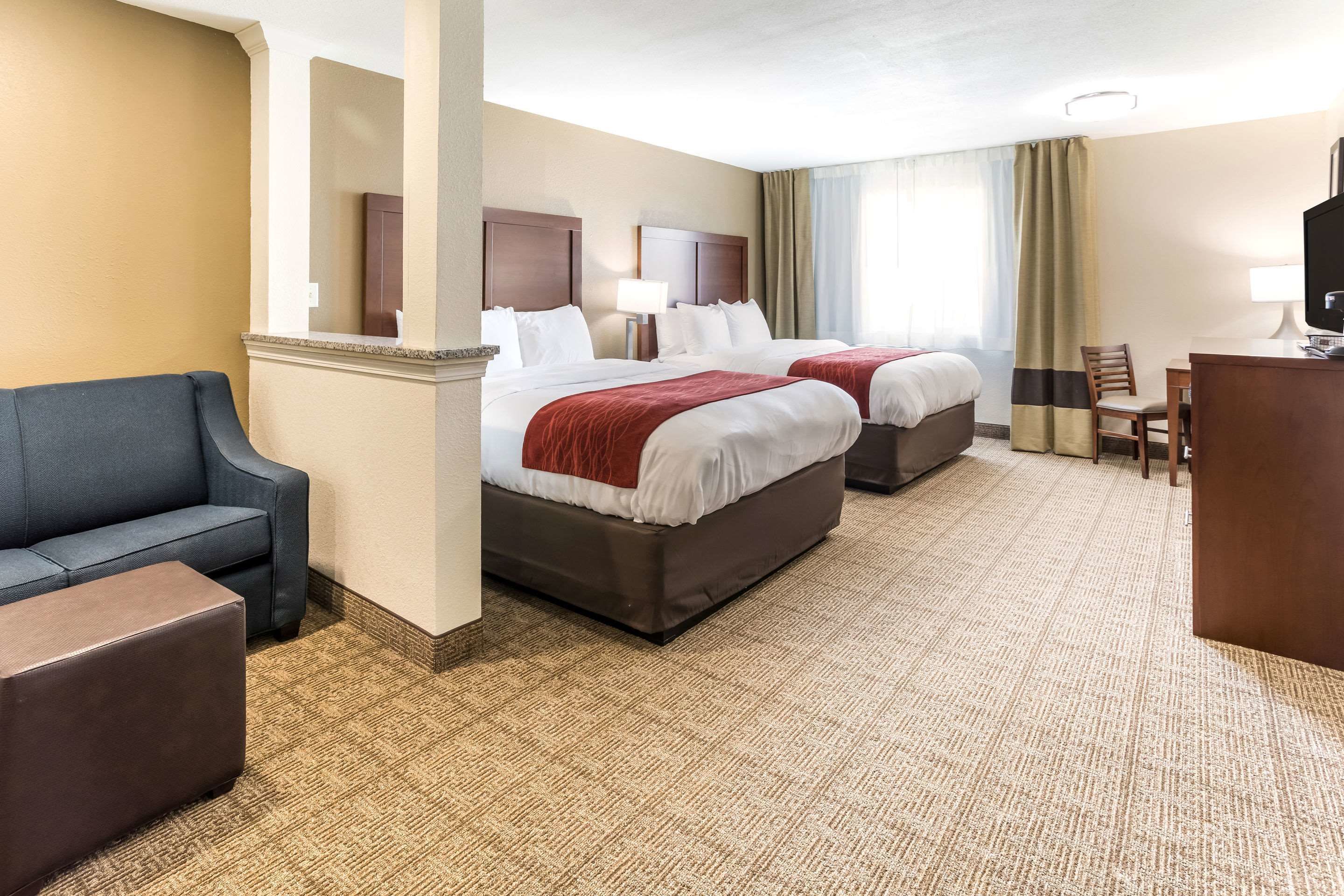 Quarto de hotel com duas camas, um sofá, uma escrivaninha e uma televisão.