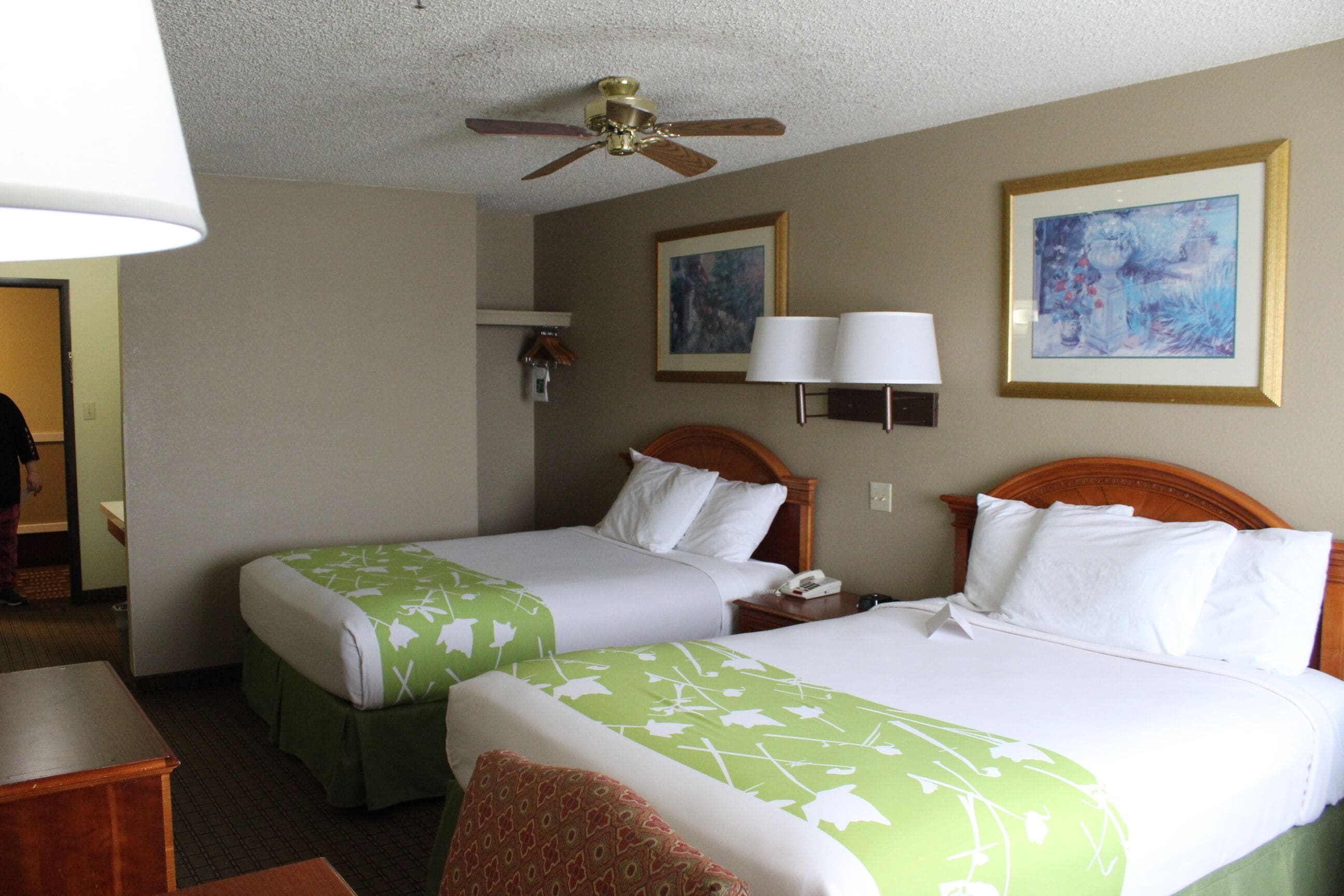 A hotel room with two beds, a ceiling fan, a desk, and a chair.