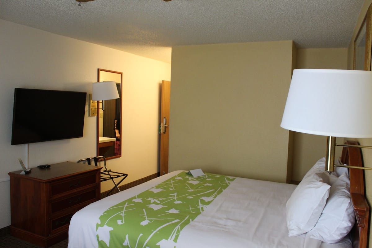 Ein Hotelzimmer mit Bett, Fernseher, Schreibtisch mit Lampe und Spiegel.