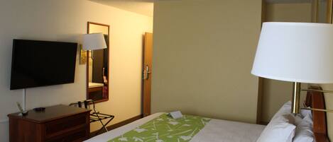 A hotel room with a bed, a television, a desk with a lamp, and a mirror.