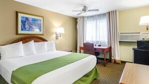 A hotel room with a bed, a desk, a chair, a ceiling fan, a window with curtains, and a wall-mounted air conditioner. - Cheyenne Guest Inn (Cheyenne)