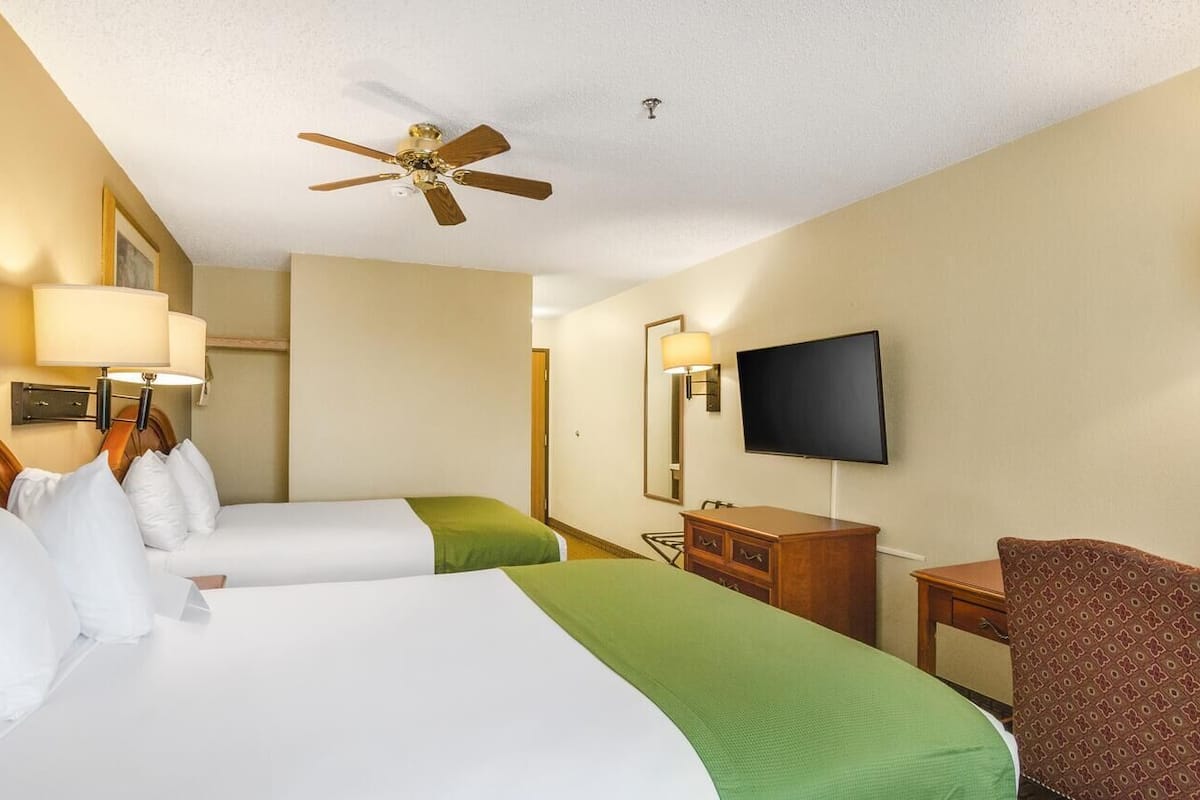 Ein Hotelzimmer mit zwei Betten, einem Deckenventilator, einem Fernseher, einem Schminktisch und einem Sessel.