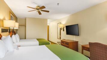 Una habitación de hotel con dos camas, un ventilador de techo, un televisor, un aparador y una silla.