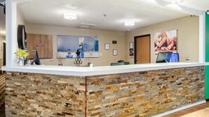 A reception area with a white counter, a wooden accent wall, and a large framed picture of a beach scene. - Cheyenne Guest Inn (Cheyenne)
