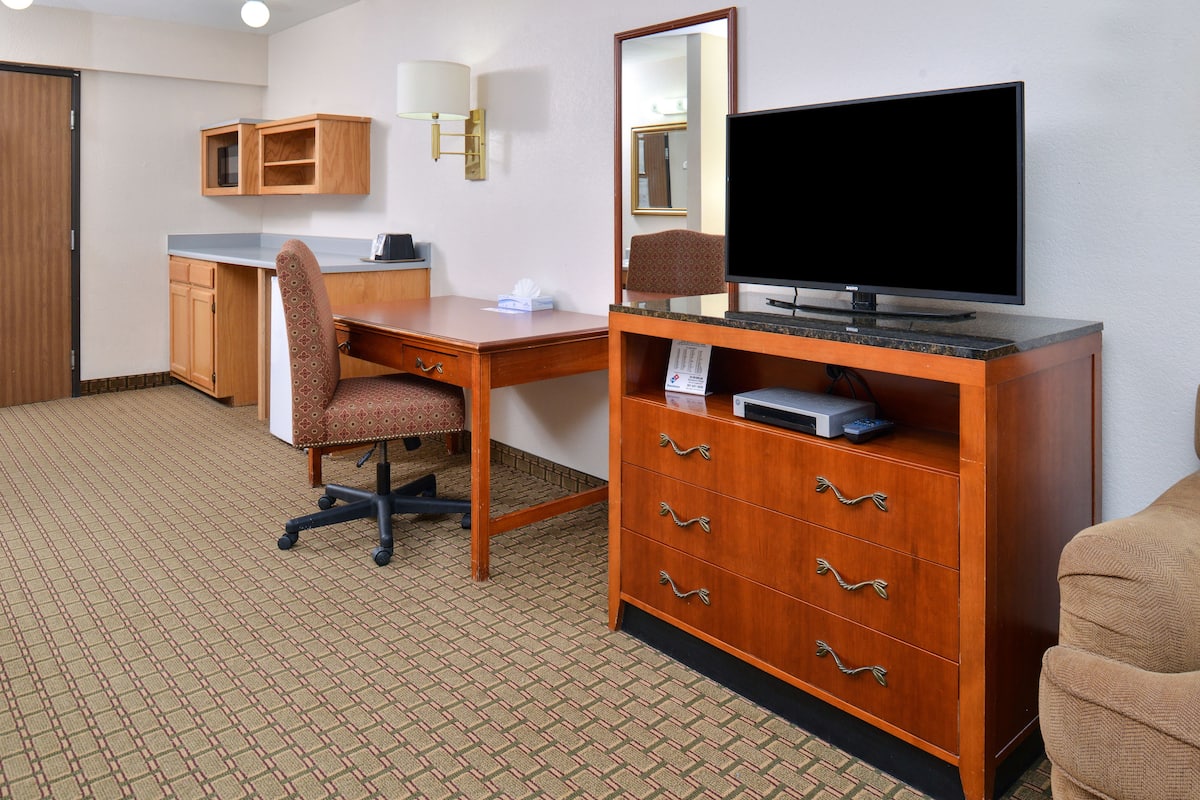 Ein Hotelzimmer mit einem Holztisch, einem Stuhl, einem Fernseher, einem Spiegel und einem Schrank.
