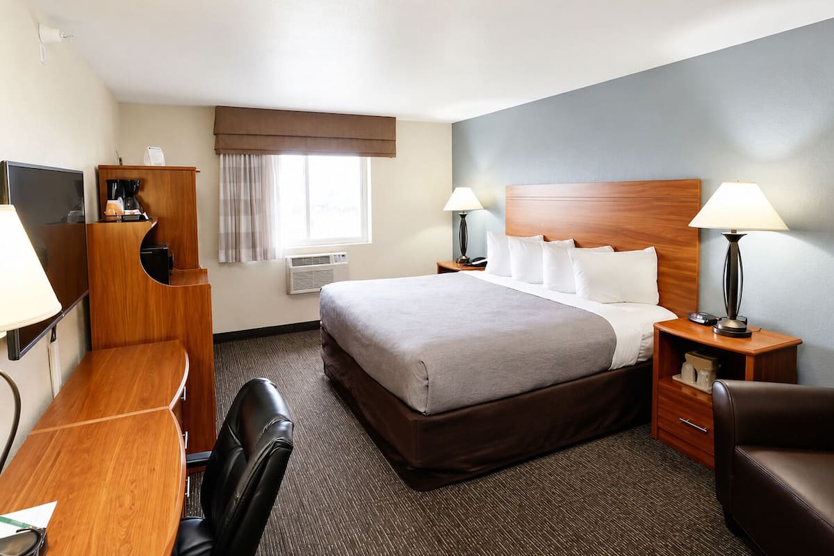 Une chambre d’hôtel avec un lit, un bureau, une chaise, des lampes et une fenêtre avec des rideaux.