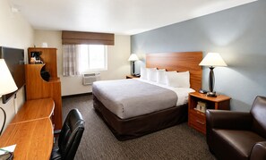 A hotel room with a bed, desk, chair, lamps, and a window with curtains.
