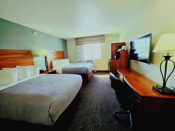 A hotel room with two beds, a desk, a chair, a TV, and a window.