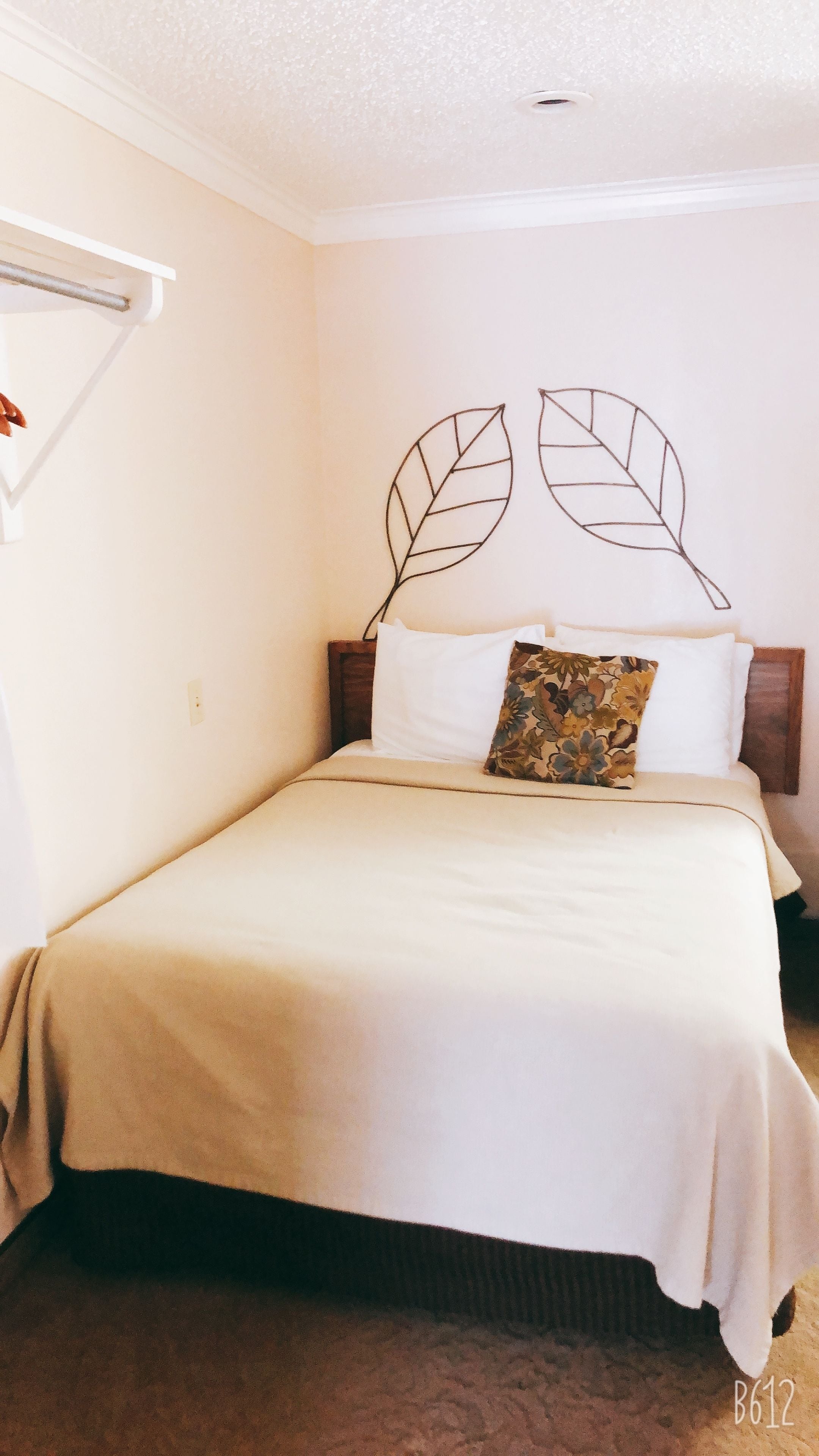 Una cama individual con cabecera en forma de hoja, ropa de cama blanca y alfombra marrón.