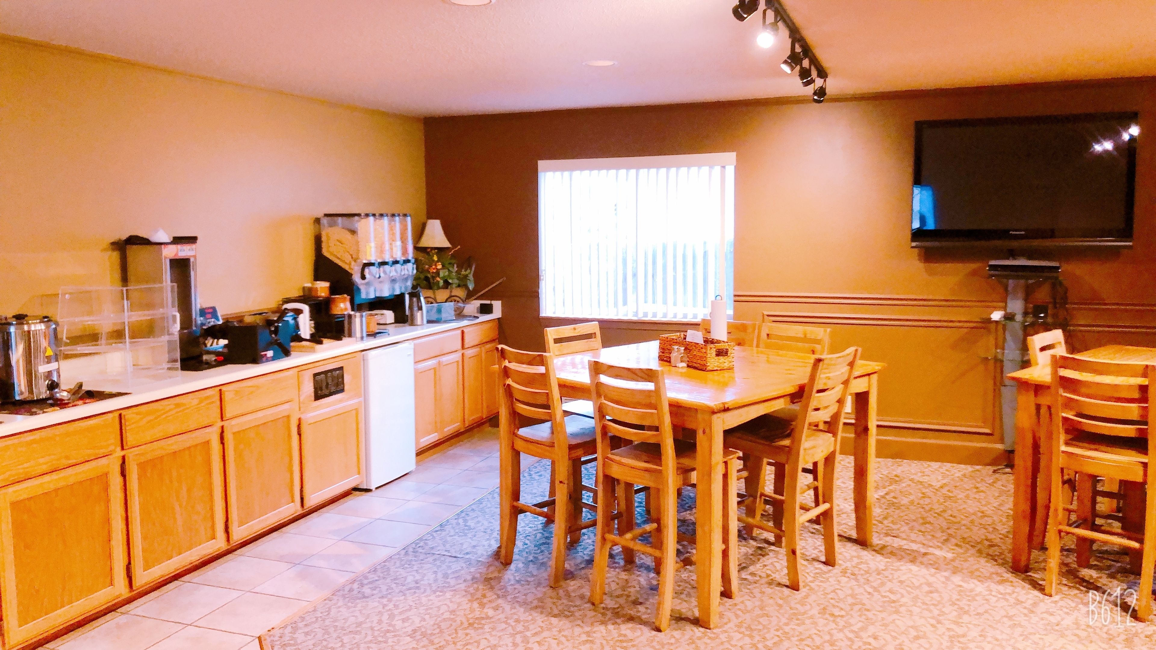 Una cocina con armarios de madera, una mesa de comedor con sillas, un refrigerador y un televisor montado en la pared.