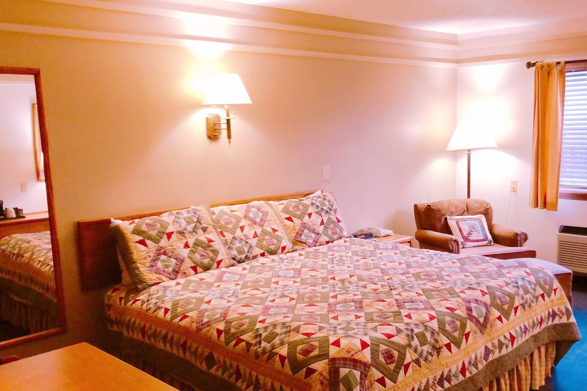 A hotel room with a large bed, two bedside lamps, a chair, a desk, and a window with curtains.