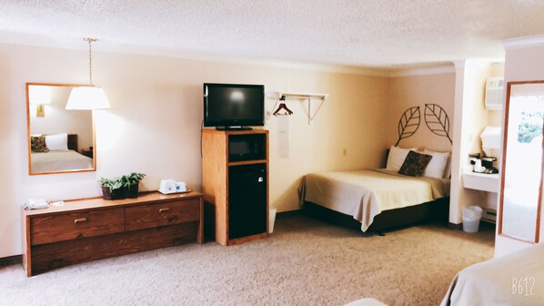 A bedroom with a bed, a dresser, a television on a stand, a mirror, and a wall-mounted shelf. - Covered Wagon Motel (Lusk)