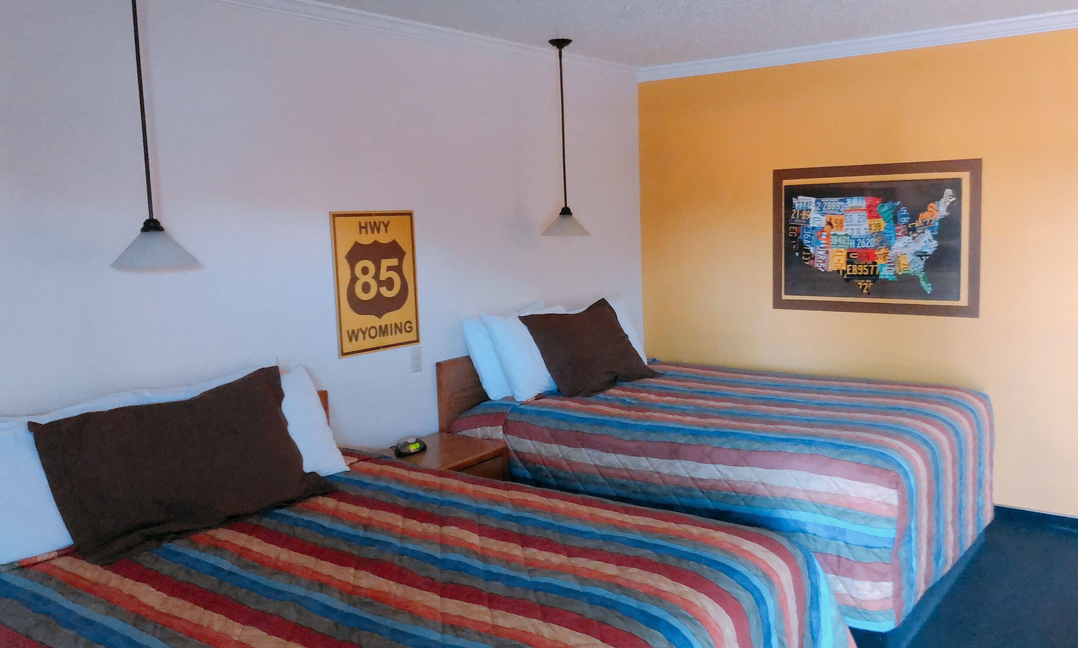 A hotel room with two beds, a map on the wall, and a sign for Highway 85 Wyoming.