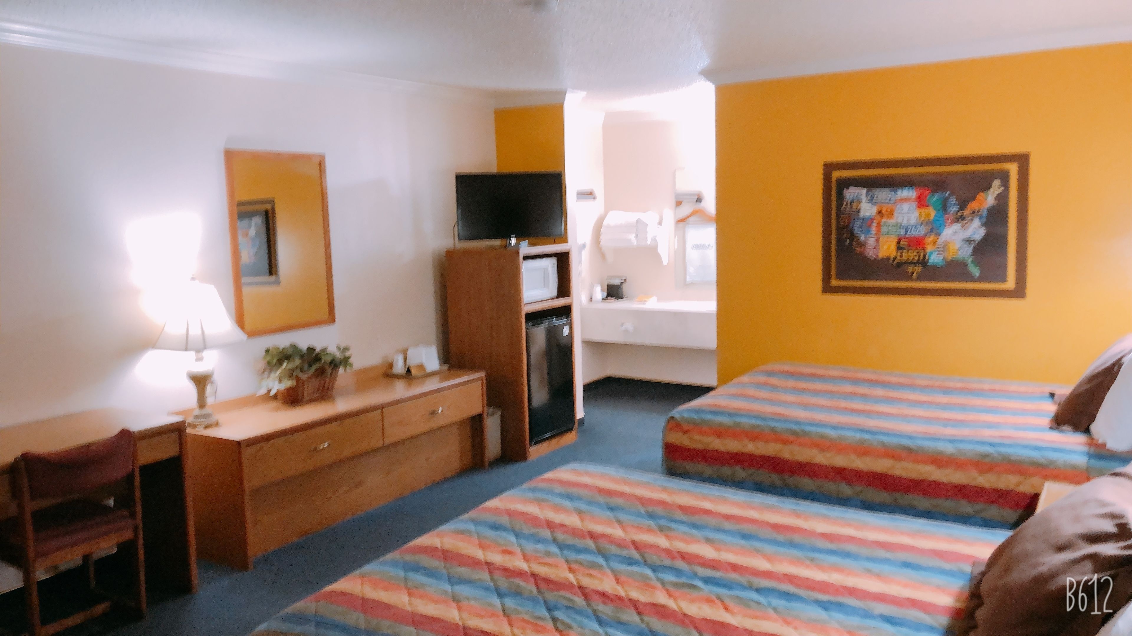 Habitación de hotel con dos camas, un escritorio, una silla, televisor, microondas y refrigerador pequeño.