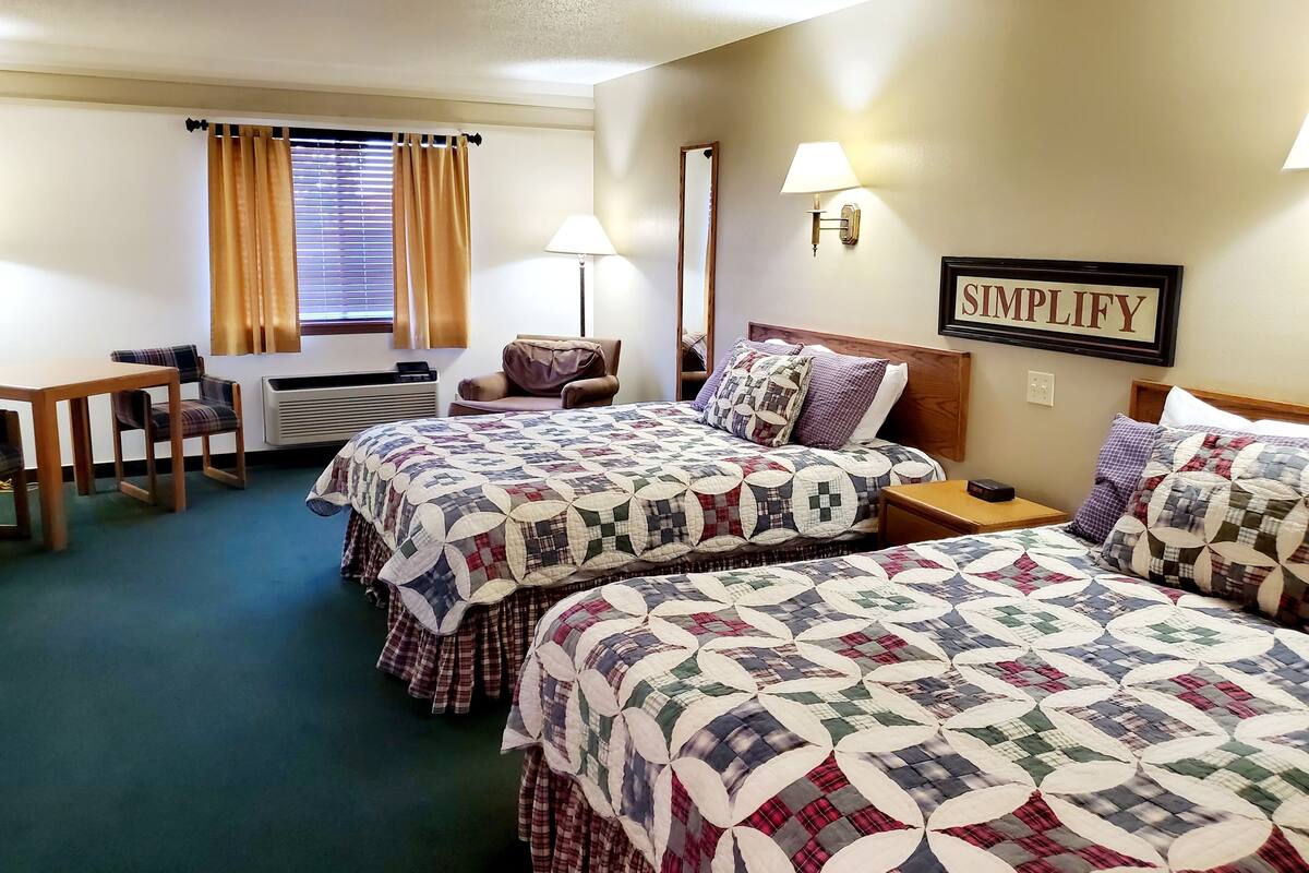 A hotel room with two beds, a desk, a chair, and a lamp.
