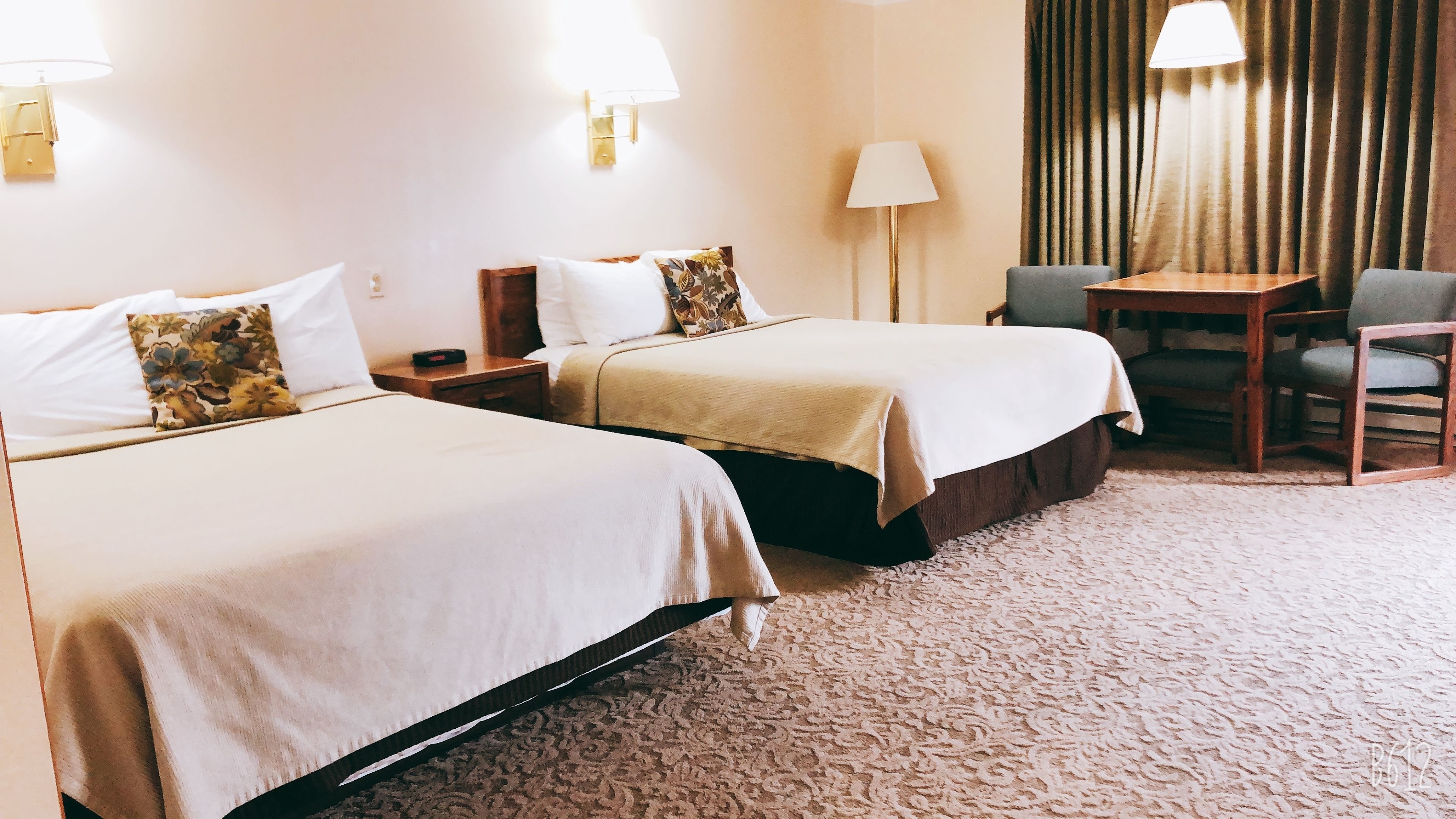 Ein Hotelzimmer mit zwei Betten, einem Schreibtisch, einem Stuhl und einer Lampe.