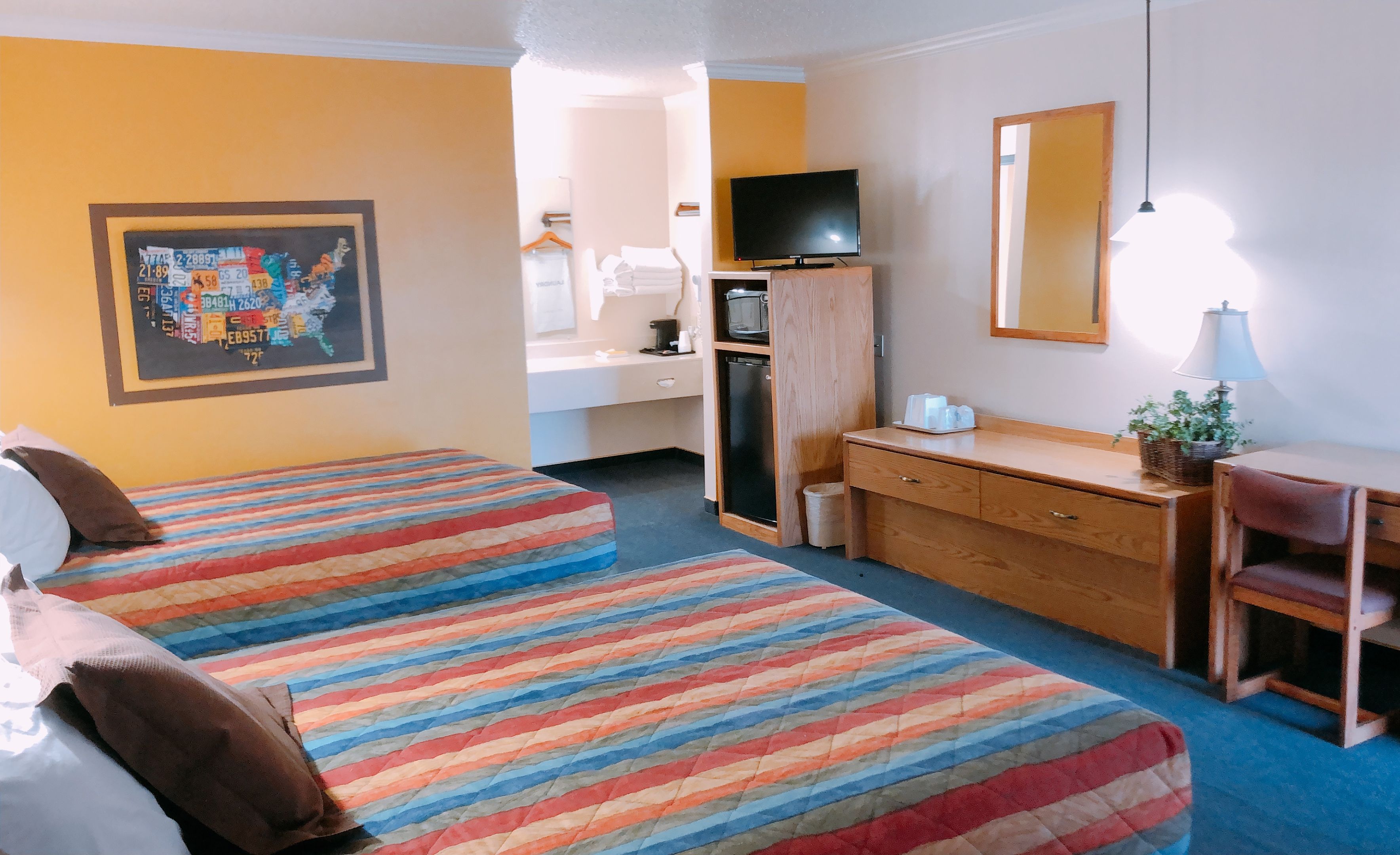 A hotel room with two beds, a desk, a television, and a mirror.