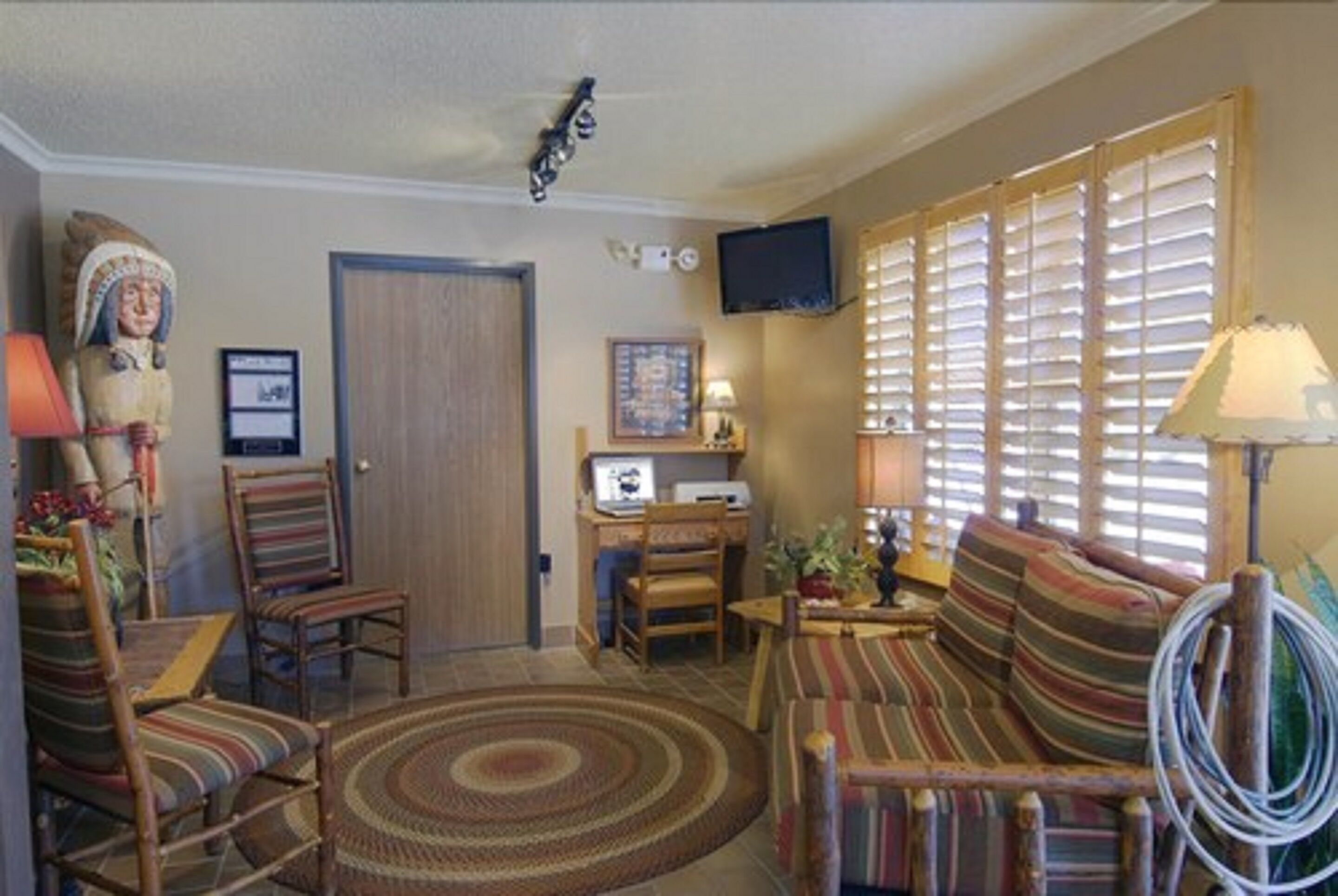 A living room with a sofa, chairs, a television, a computer, and a large window with blinds.