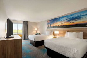 A hotel room with two beds, a TV, a desk, and a large painting of a sunset. - Days Inn by Wyndham Grand Island I-80 (Grand Island)
