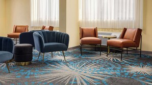 A hotel room with a blue and brown chair arrangement, a patterned carpet, and a window with sheer curtains. - Days Inn by Wyndham Grand Island I-80 (Grand Island)