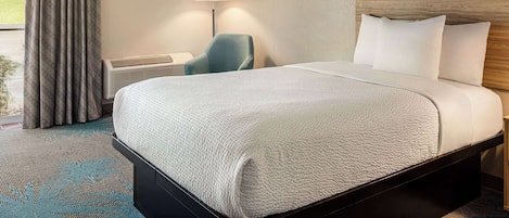 Een hotelkamer met een groot bed, een bureau, een stoel, een lamp en een schilderij van een landschap.