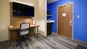A hotel room with a wooden desk, a television, a microwave, and a blue wall. - Holiday Inn Express & Suites - North Platte by IHG (North Platte)