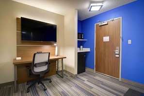 A hotel room with a wooden desk, a television, a microwave, and a blue wall. - Holiday Inn Express & Suites - North Platte by IHG (North Platte)