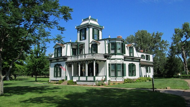 A large, white, two-story house with green trim and multiple windows, surrounded by a well-maintained lawn and trees. - Holiday Inn Express & Suites - North Platte by IHG (North Platte)