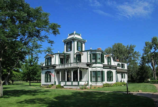 A large, white, two-story house with green trim and multiple windows, surrounded by a well-maintained lawn and trees. - Holiday Inn Express & Suites - North Platte by IHG (North Platte)