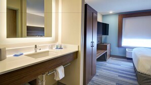 A hotel bathroom with a large mirror, a sink, a vanity, a towel rack, and a television. - Holiday Inn Express & Suites - North Platte by IHG (North Platte)