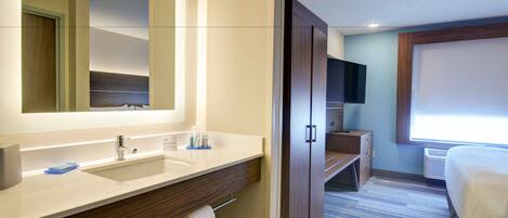 A hotel bathroom with a large mirror, a sink, a vanity, a towel rack, and a television.