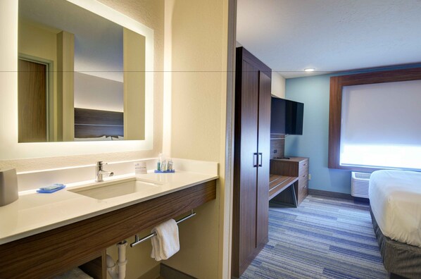 A hotel bathroom with a large mirror, a sink, a vanity, a towel rack, and a television.