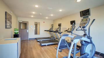 Ein Fitnessstudio mit Laufbändern, Crosstrainern und einer Spiegelwand.