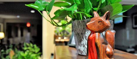 Une figurine de renard en bois, posée sur une surface en bois, avec une plante en pot derrière.