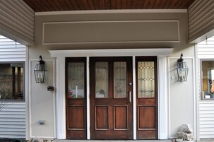 Puerta principal con dos paneles de vidrio y madera, flanqueada por dos lámparas de estilo farol.