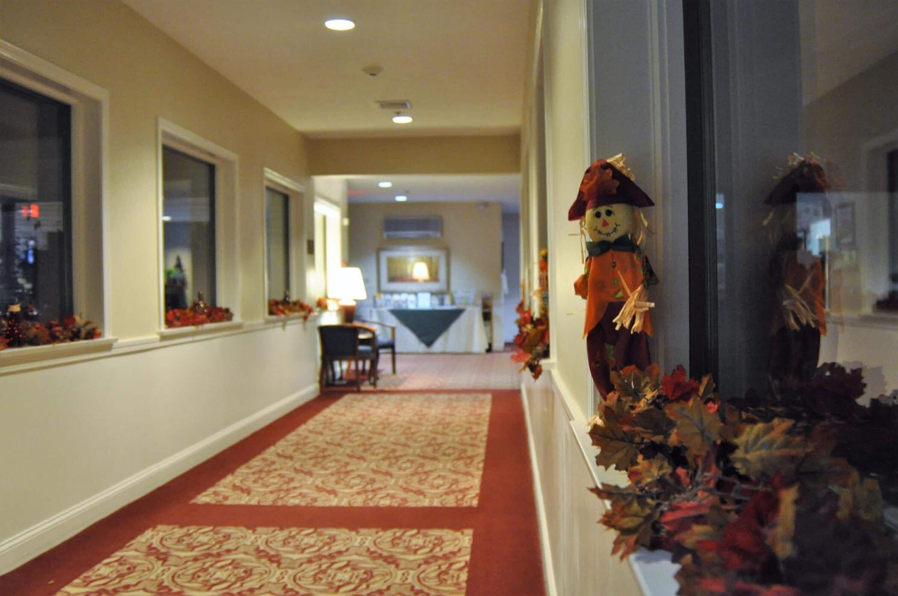 Un couloir d’hôtel avec un tapis à motifs, un coin repas en arrière-plan et des décorations sur le thème de l’automne.