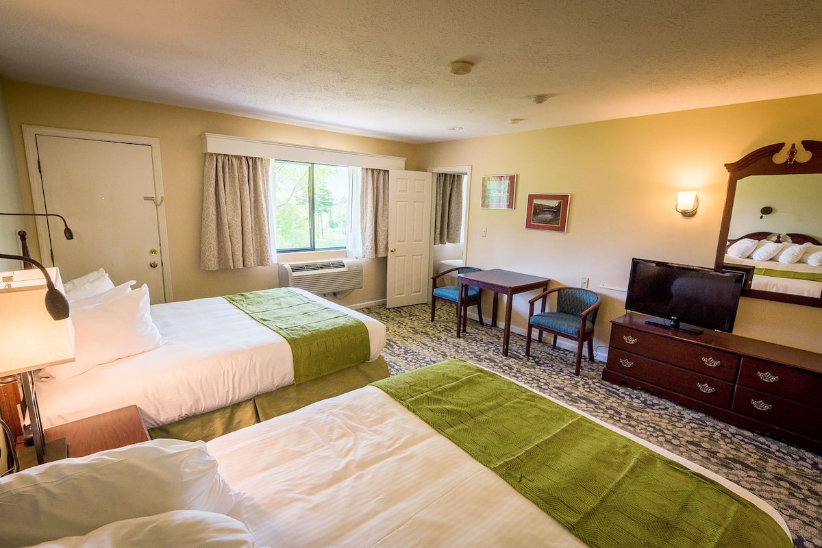 A hotel room with two beds, a desk, a chair, a television, and a dresser.